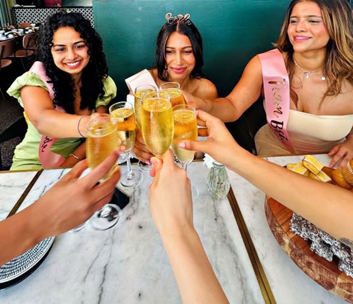 Friends in sashes clinking glasses of bubbles across a table