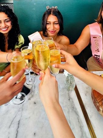 Hens in sashes and a tiara clinking glasses of bubbles across the table