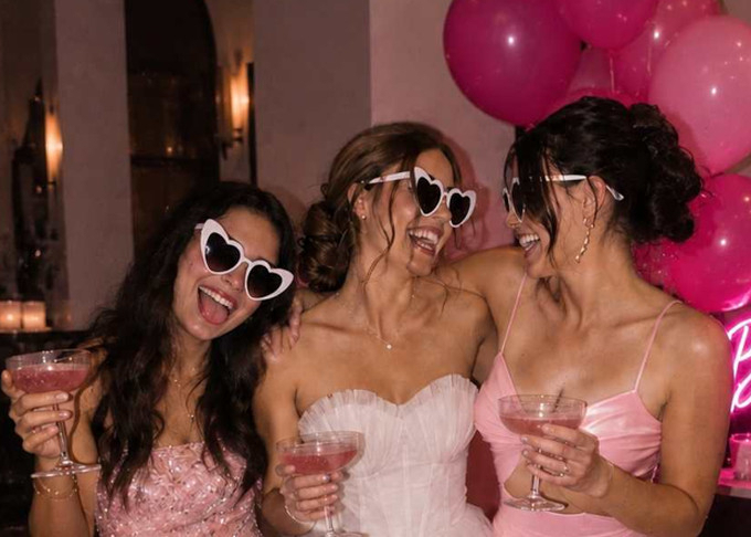 Three friends in heart sunglasses clinking pink cocktails
