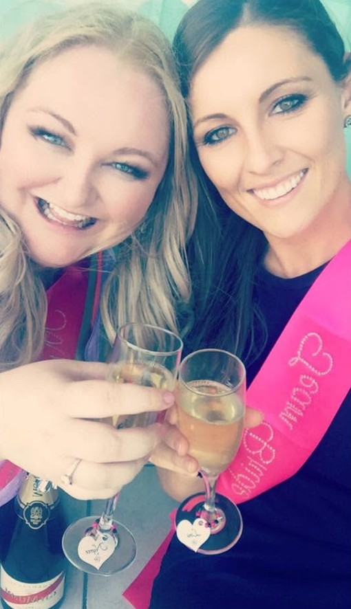 Two friends in pink sashes smiling in a selfie with glasses of bubbly