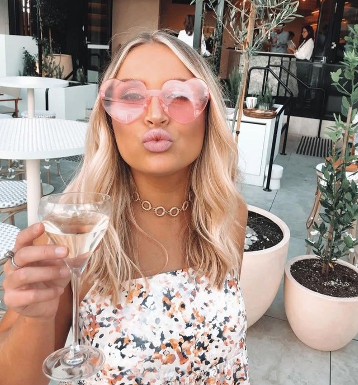 A friend in pink heart sunglasses blowing a kiss with a glass of bubbly
