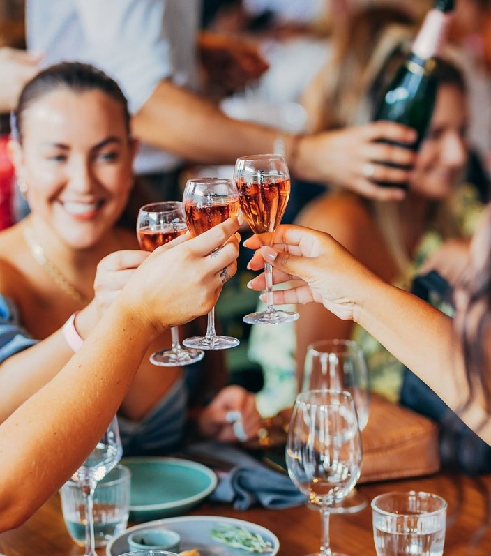 Friends clinking glasses of rose bubbles across the table
