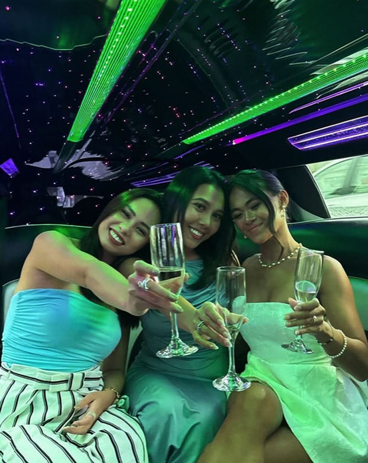 Three friends raising champagne flutes in the back of a limousine under coloured lights