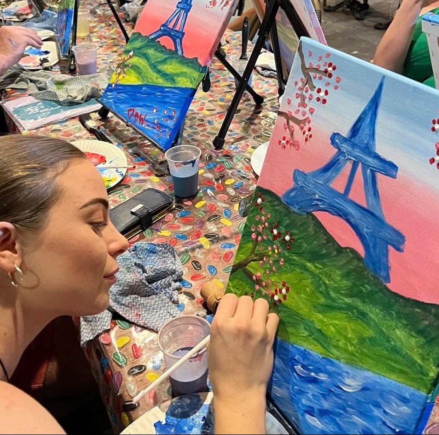 A guest leaning in to paint cherry blossoms around a pink and blue Eiffel Tower