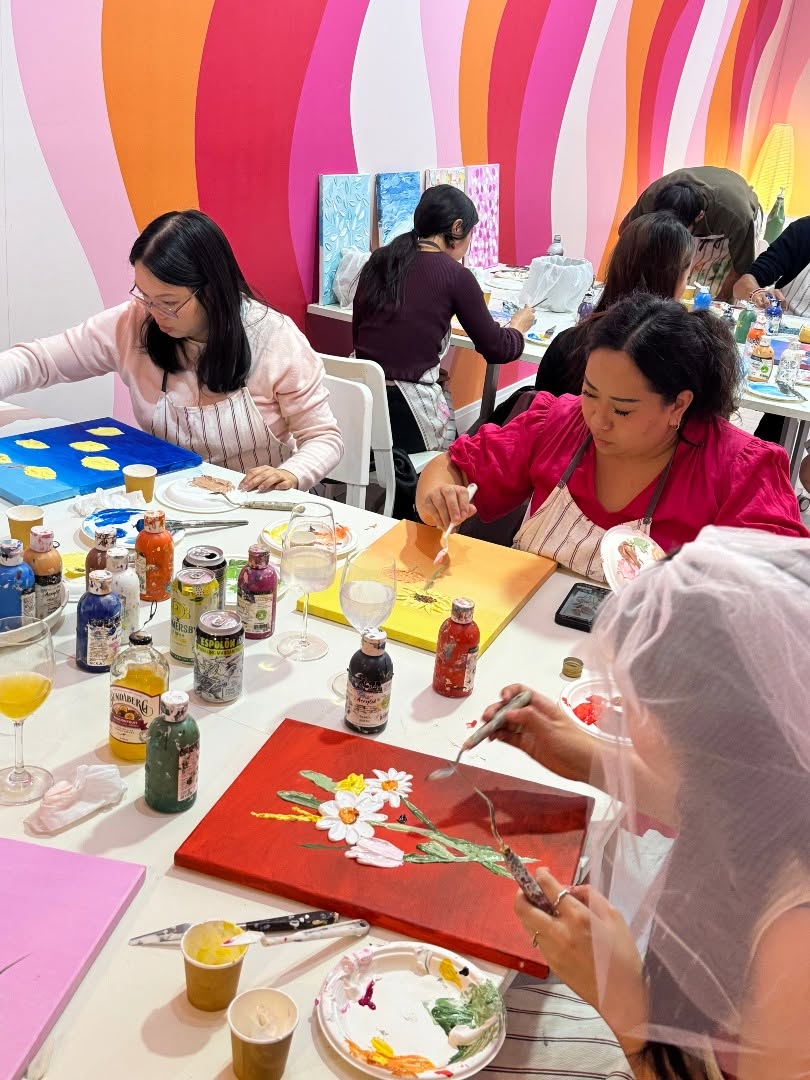 The bride in her veil painting white daisies on a red canvas, her friends painting beside her