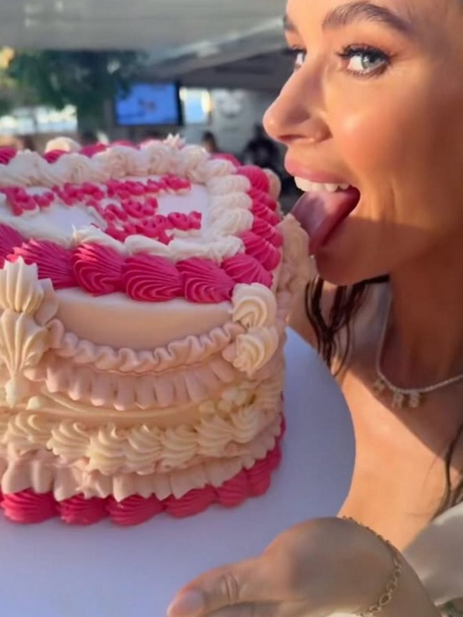 A woman tasting the icing on a pink and white heart-shaped cake