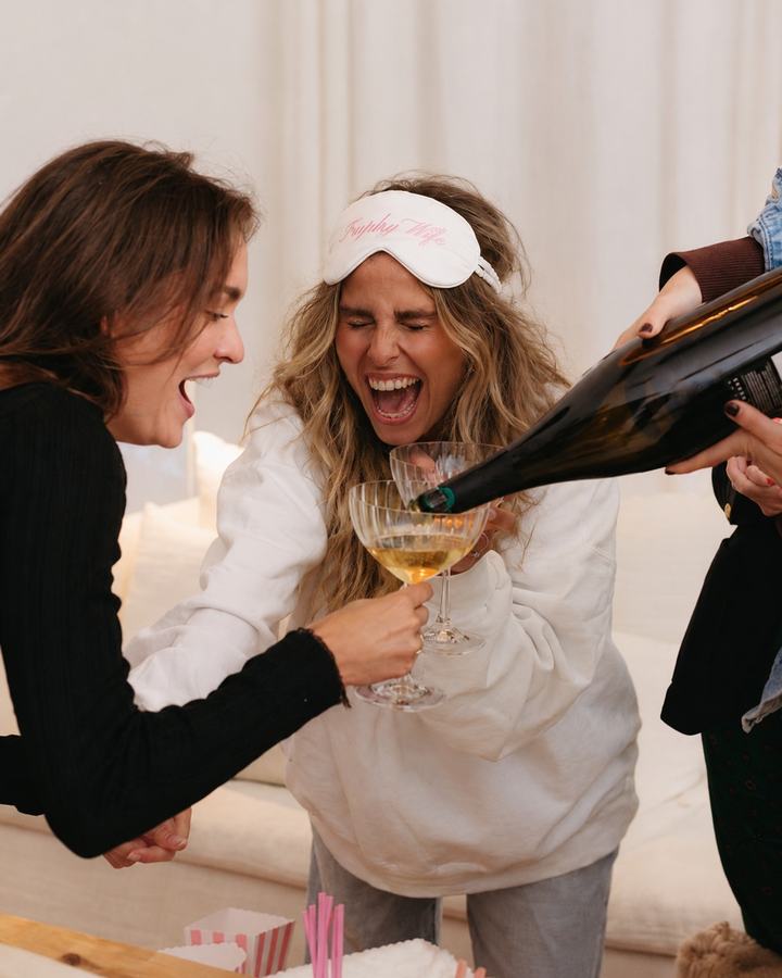Two friends in pyjamas and eye masks laughing as champagne is poured