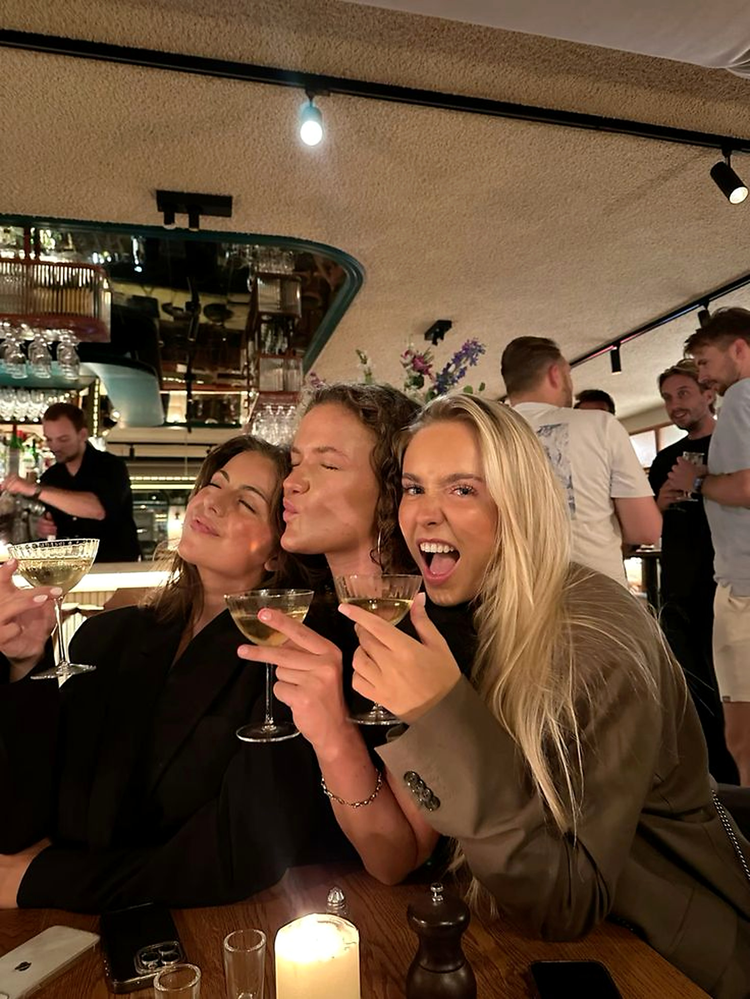 Three friends laughing together at a bar at night, glasses raised