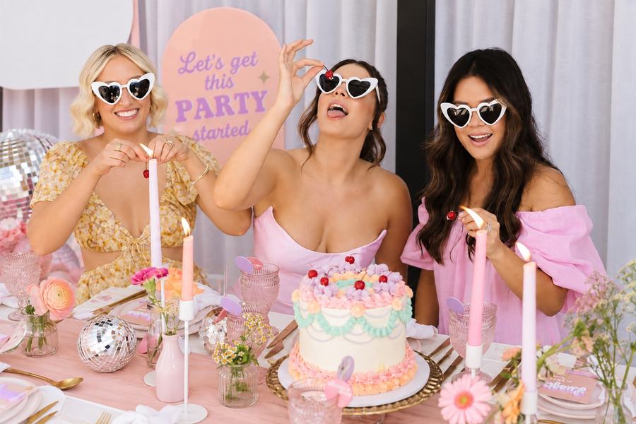 Three friends in heart-shaped sunglasses behind a decorated cake
