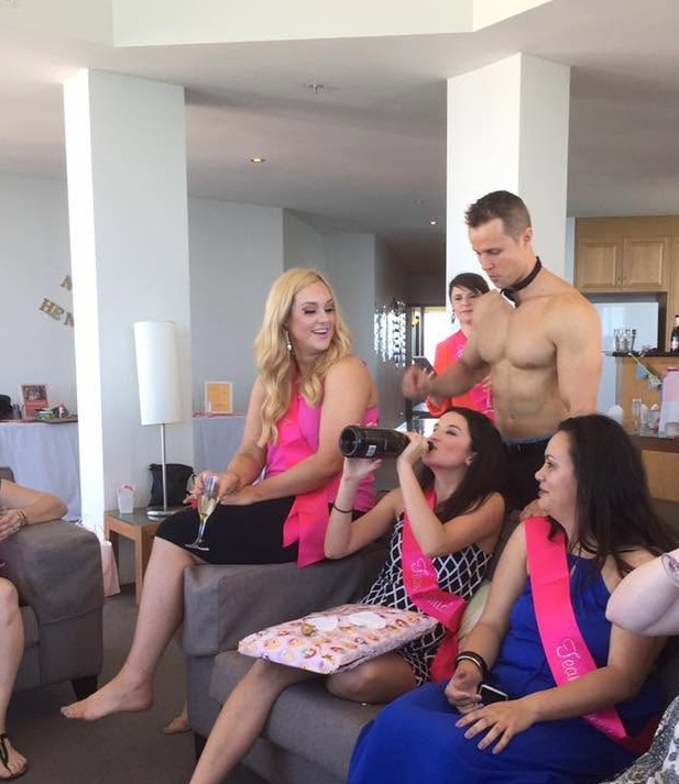 Hens in pink sashes on an apartment couch with our topless waiter in his bow tie standing behind them