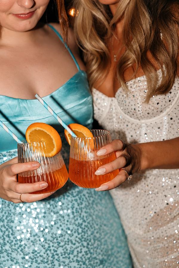 Two friends in sequin dresses holding orange cocktails