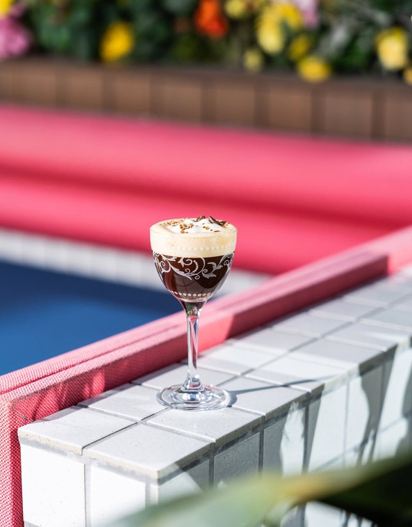 A cocktail on a tiled ledge beside a pink banquette in the sun