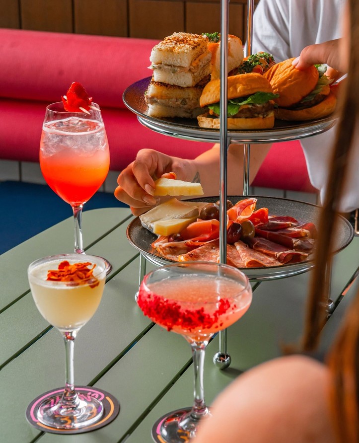Cocktails beside a high tea stand of sandwiches, cheese and cured meats