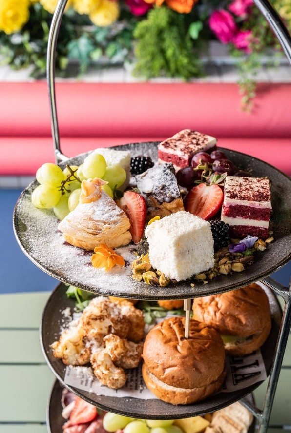 A tiered stand of sweets, sliders and fruit in front of a pink banquette and bright flowers