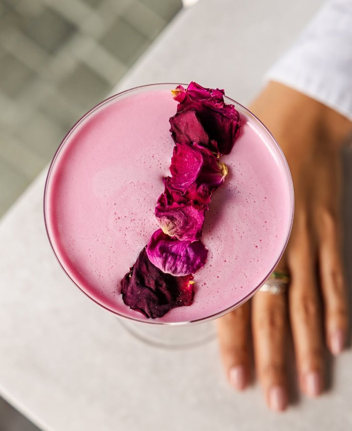 A pink cocktail topped with dried rose petals