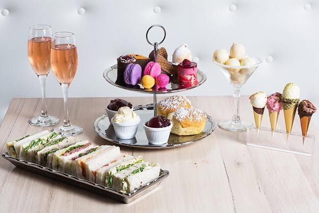 Rose bubbles, ribbon sandwiches, a two-tier stand of scones and sweets, and little ice cream cones on a table