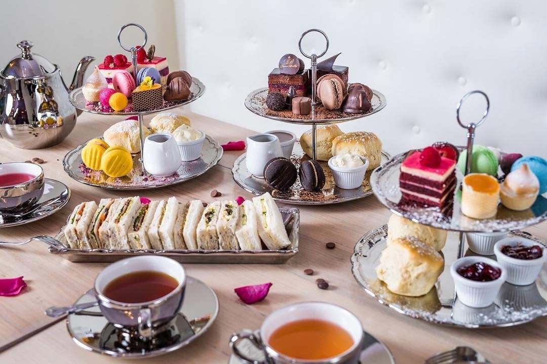 A table of three tiered stands with scones, jam and cream, sandwiches and sweets, and cups of tea