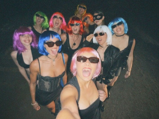 A whole crew in bright coloured wigs and sunglasses squeezing into one night-time selfie