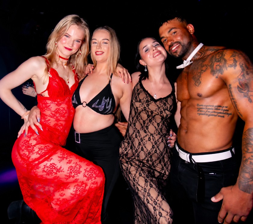 Three guests posing with a shirtless male revue performer in a bow-tie collar