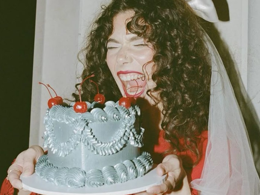 Someone in a veil laughing behind a cherry-topped cake