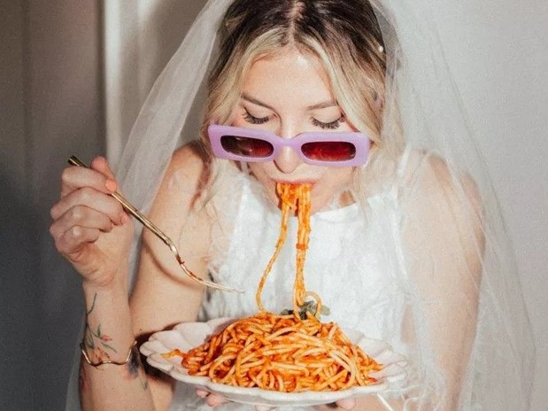 Someone in a veil and lilac sunglasses slurping a forkful of spaghetti