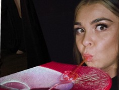 Britt sipping a pink cocktail through a straw from a giant glass