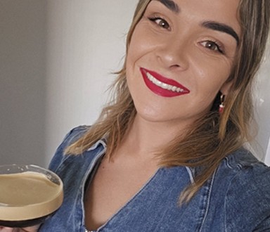 Britt in a denim jacket with red lipstick, holding up a creamy coffee cocktail