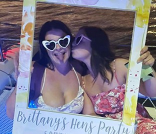 Britt and a friend in heart sunglasses behind her hens party photo frame, which reads Brittany’s Hens Party, 5 days until I do