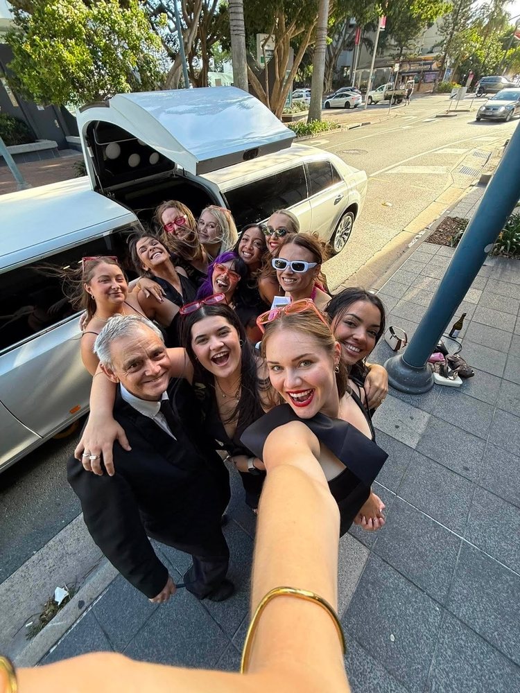 A big group selfie of the hens in front of a white stretch limo