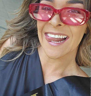 Britt in pink sunglasses and a black hens sash, poking her tongue out for a selfie