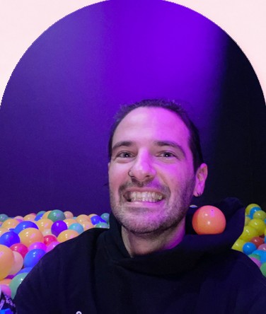 James grinning in a ball pit full of coloured balls under purple light