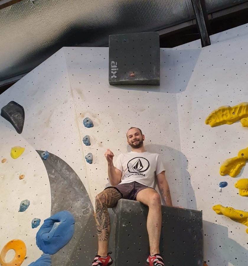 Josh sitting on top of a bouldering block at an indoor climbing wall, giving a thumbs up