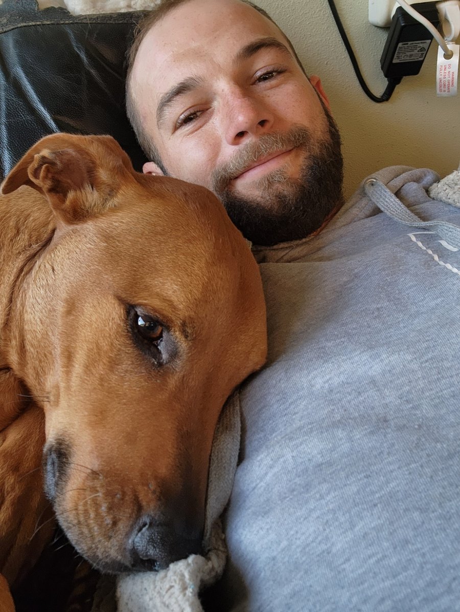 Josh lying on the couch with a brown dog resting its head on his chest