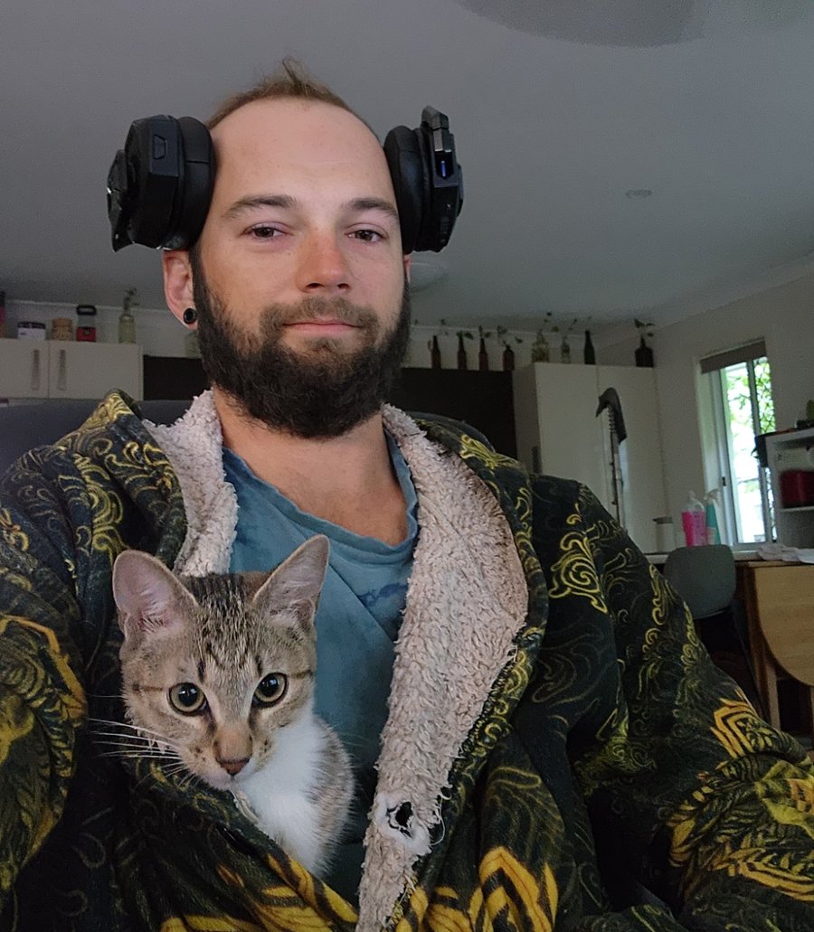 Josh with headphones pushed up on his head and a kitten peeking out of his robe