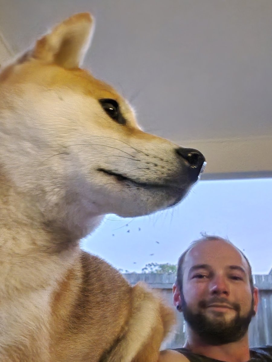 A Shiba Inu dog filling most of a selfie, with Josh smiling in the corner