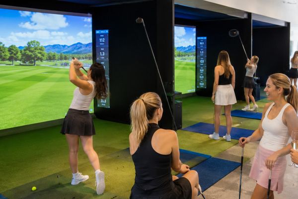 Group of friends take turns swinging at a big golf simulator screen
