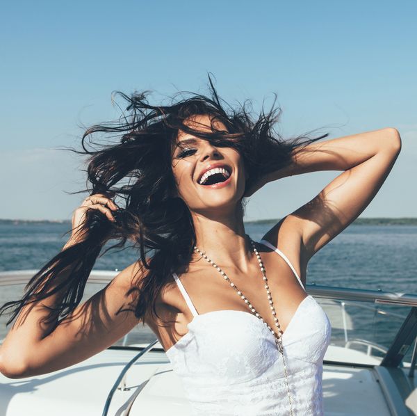 A woman in white laughing with her hair blowing on the deck of a boat