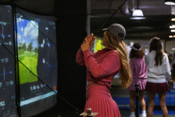 Woman in a pink pleated skirt takes a swing at a golf simulator screen