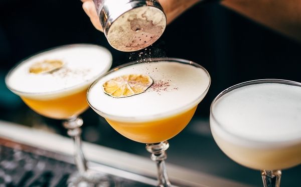 Three cocktail drinks topped with chocolate powder and lemon slices at the bar counter during the cocktail making class