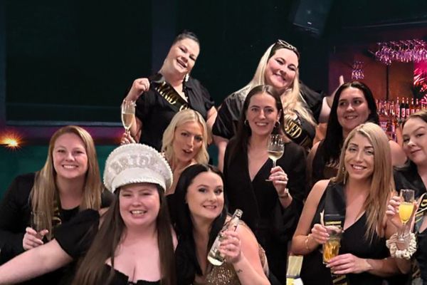 Hens group in black with the bride in a white hat, glasses raised
