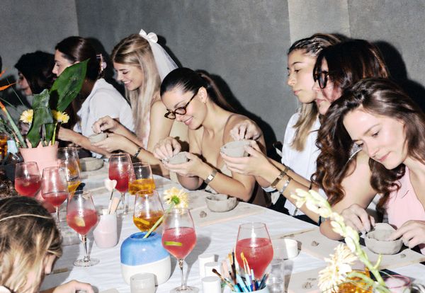 The bride in a veil and her friends shaping little clay pots along a long table with cocktails and flowers