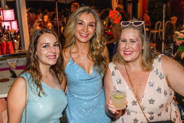 Three friends smiling together with drinks at a busy Darlinghurst bar at night