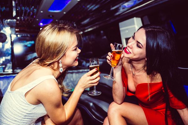 Two friends laughing and toasting with drinks inside a limousine