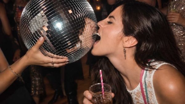 A woman biting a disco ball with a drink in her other hand