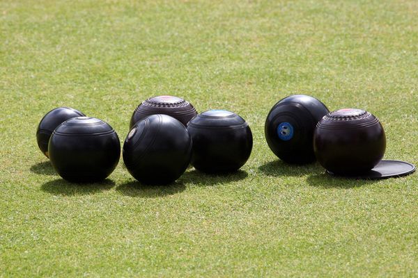 Black lawn bowls and a jack resting on a closely mown bowling green
