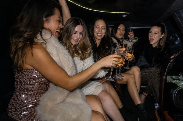 Friends in sequins and faux fur laughing and toasting in the back of a party bus