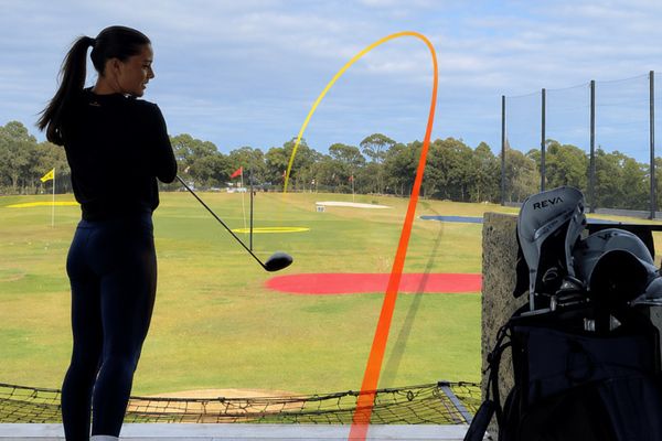 Woman driving a golf ball down the range, its flight traced in orange