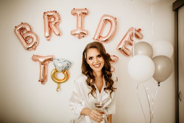 Hen dressed in white robes poses for a photo with balloons as a backdrop