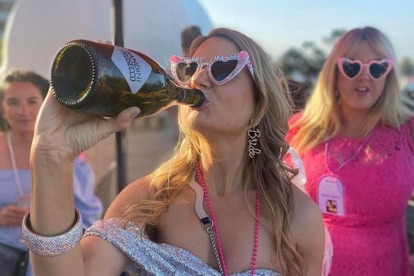 Bride in heart sunglasses drinking from a bubbly bottle beside a friend in pink