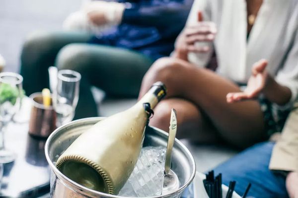 A bottle of bubbles chilling in an ice bucket as friends chat
